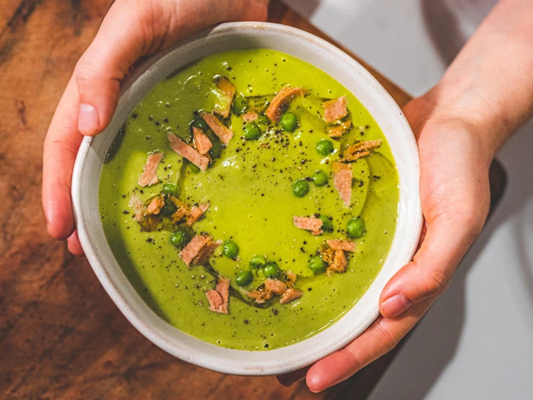 Vegan Pea And Ham soup served in a white bowl with ham trimmings on the top.