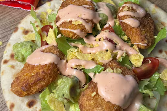 Quorn Cheesy Nacho Nuggets on an open flatbread with lettuce, chopped cherry tomatoes and drizzled with taco sauce.