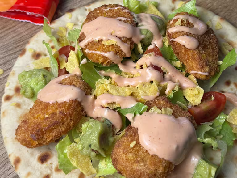 Quorn Cheesy Nacho Nuggets on an open flatbread with lettuce, chopped cherry tomatoes and drizzled with taco sauce.