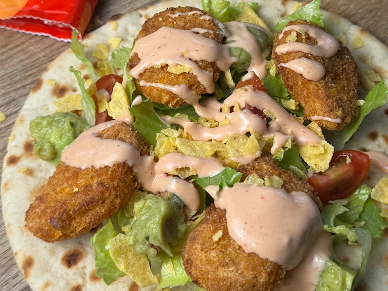 Quorn Cheesy Nacho Nuggets on an open flatbread with lettuce, chopped cherry tomatoes and drizzled with taco sauce.
