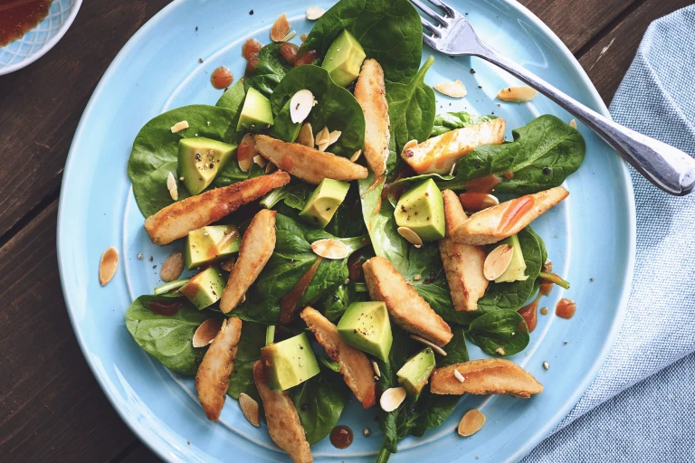 A spinach salad topped with diced avocado, sliced Quorn Fillets, dressing, and toasted almonds.