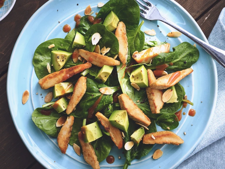 A spinach salad topped with diced avocado, sliced Quorn Fillets, dressing, and toasted almonds.