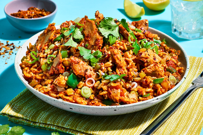 A white bowl of jambalaya rice make with Quorn Roasted Sliced Fillets on a bright turquoise background.