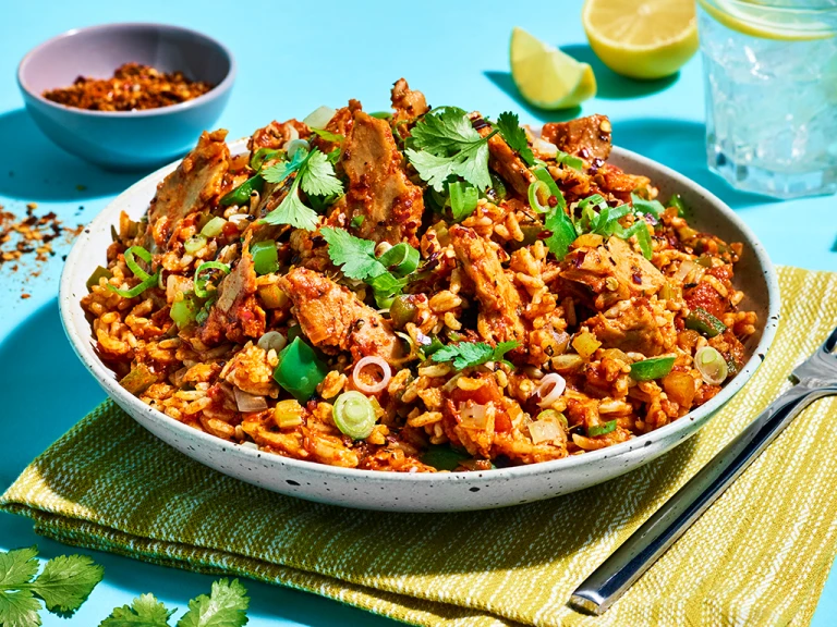 A white bowl of jambalaya rice make with Quorn Roasted Sliced Fillets on a bright turquoise background.