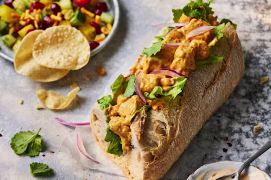 Half of a Quorn Vegetarian Chicken Tikka Baguette Sandwich with the filling visible topped with red onions.