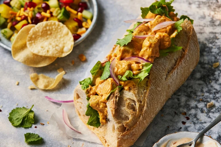 Half of a Quorn Vegetarian Chicken Tikka Baguette Sandwich with the filling visible topped with red onions.  