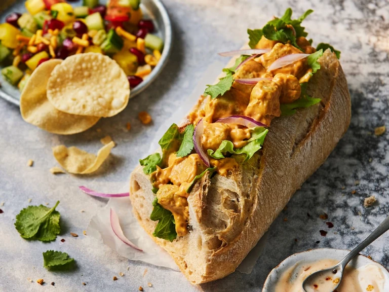 Half of a Quorn Vegetarian Chicken Tikka Baguette Sandwich with the filling visible topped with red onions.  