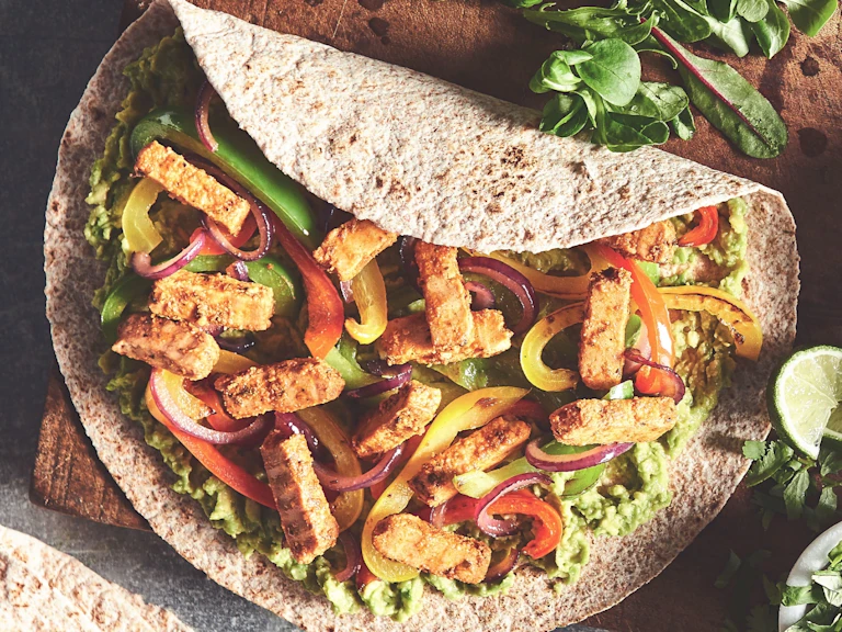 Quorn Smoky Fajita Strips, peppers, onions, and guacamole on a tortilla.