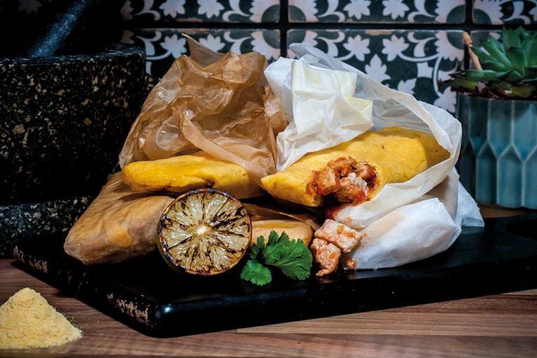 Mexican-style tamales made with Quorn Pieces wrapped in paper piled next to a molcajete with charred citrus and fresh coriander on the side.