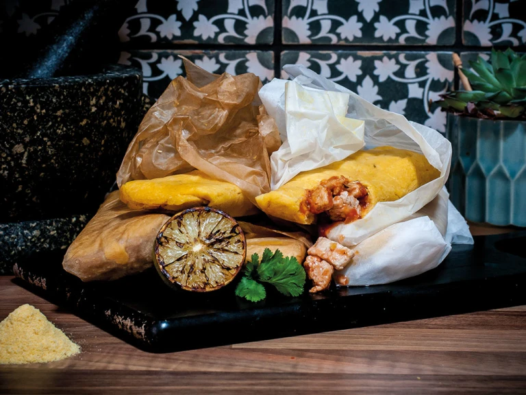 Mexican-style tamales made with Quorn Pieces wrapped in paper piled next to a molcajete with charred citrus and fresh coriander on the side.