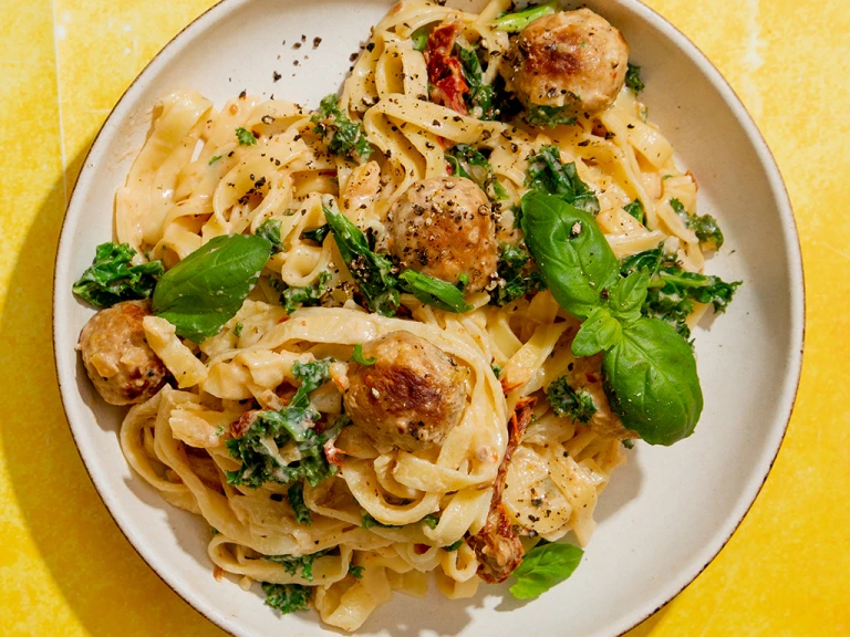 Quorn Swedish Style Balls in a creamy tomato sauce with kale and basil served on tagliatelle pasta in a bowl on a yellow background.