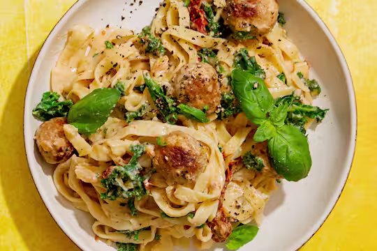Quorn Swedish Style Balls in a creamy tomato sauce with kale and basil served on tagliatelle pasta in a bowl on a yellow background.