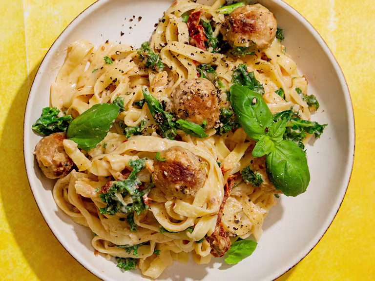 Quorn Swedish Style Balls in a creamy tomato sauce with kale and basil served on tagliatelle pasta in a bowl on a yellow background.
