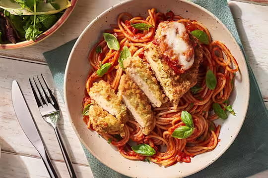 Dish with Quorn Mozzarella and Pesto Escalope parmigiana and basil alongside side dishes of salad and olives