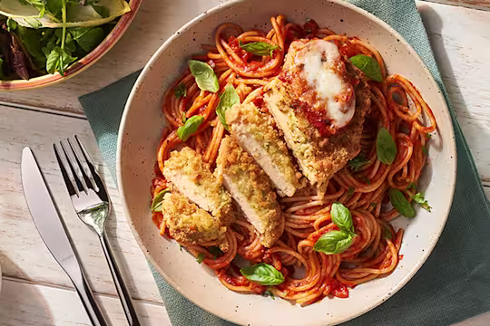 Dish with Quorn Mozzarella and Pesto Escalope parmigiana and basil alongside side dishes of salad and olives