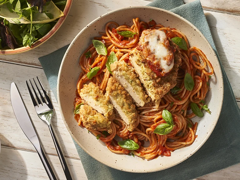 Dish with Quorn Mozzarella and Pesto Escalope parmigiana and basil alongside side dishes of salad and olives