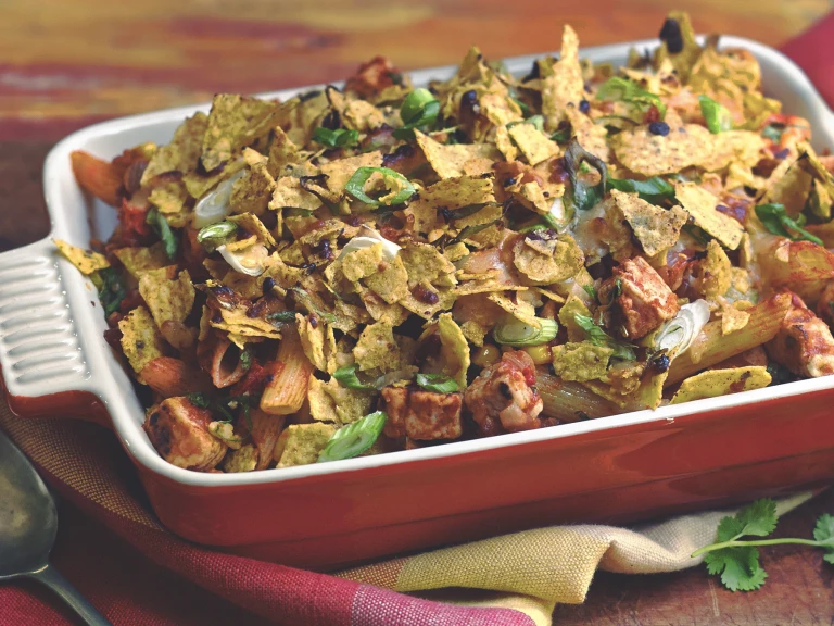 Penne pasta topped with bell pepper, tomatoes, corn, jalapenos, green onions, cheese, tortilla chips, and Quorn Pieces in an orange dish.