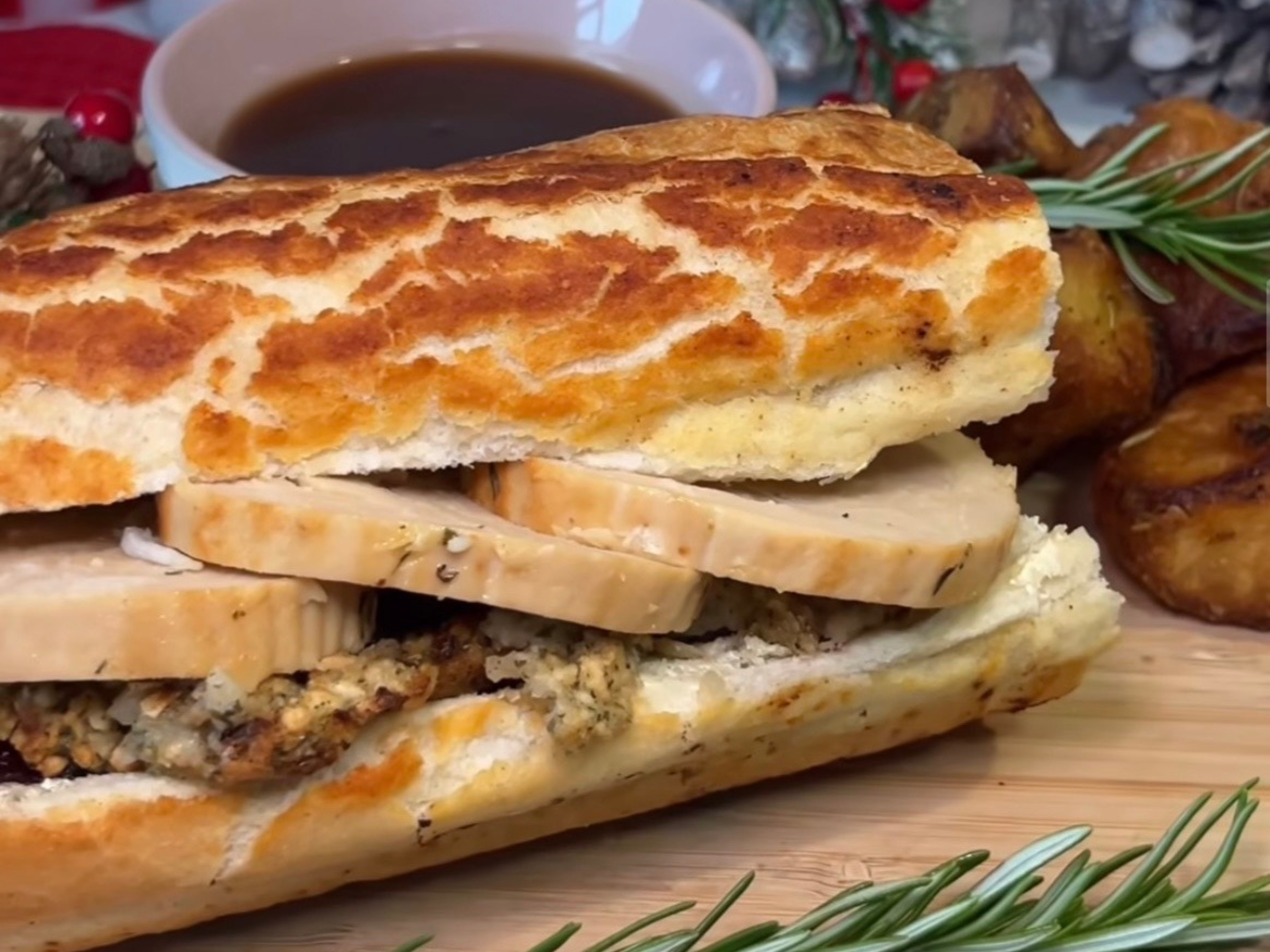 A Quorn Christmas Roast & Stuffing Baguette on a wooden board with a bowl of gravy.