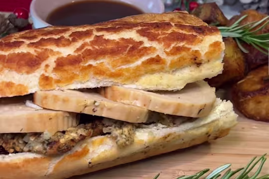 A Quorn Christmas Roast & Stuffing Baguette on a wooden board with a bowl of gravy.