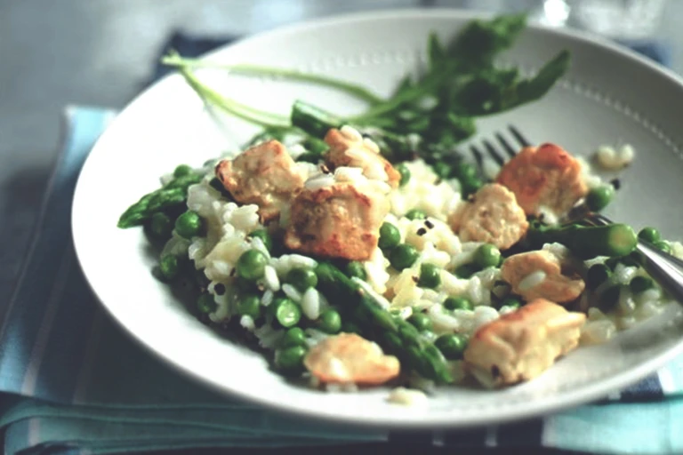 Risotto with peas, asparagus, and Quorn Pieces garnished with basil in a white bowl.