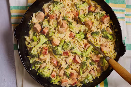 A large portion of Quorn Vegetarian Sausage and Broccoli Orzo served in a dark dish with a serving spoon.