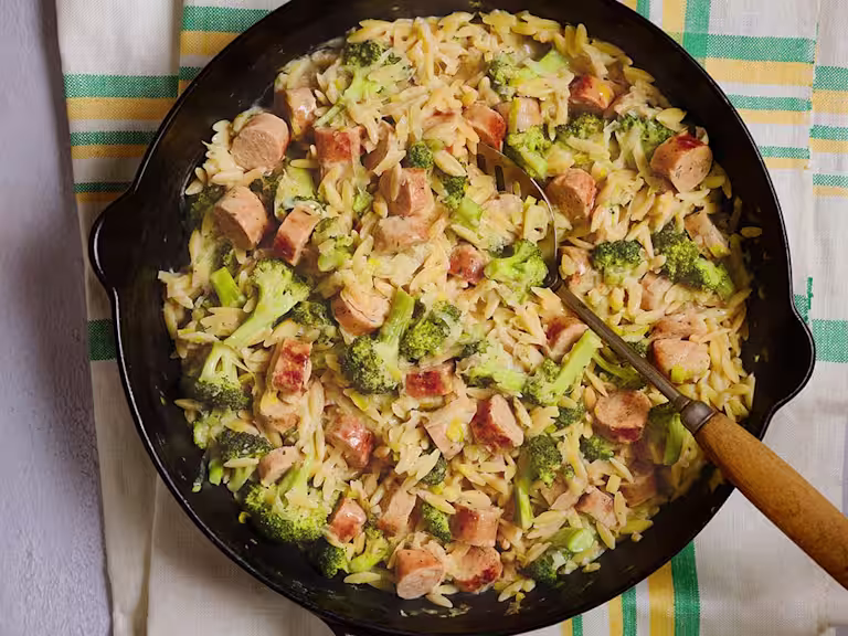 A large portion of Quorn Vegetarian Sausage and Broccoli Orzo served in a dark dish with a serving spoon.