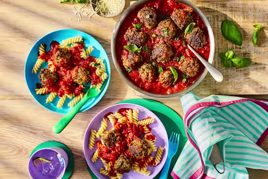 Meatballs in a rich tomato sauce served with fusilli pasta and fresh basil leaves.