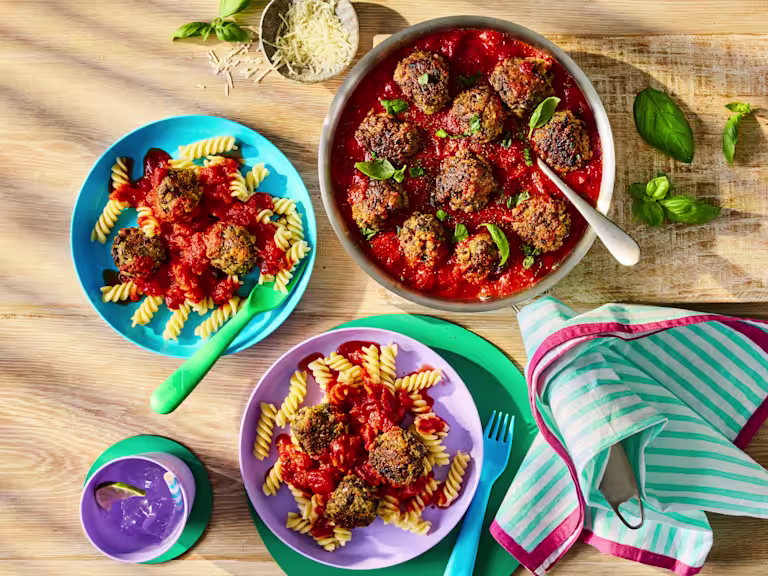 Meatballs in a rich tomato sauce served with fusilli pasta and fresh basil leaves.