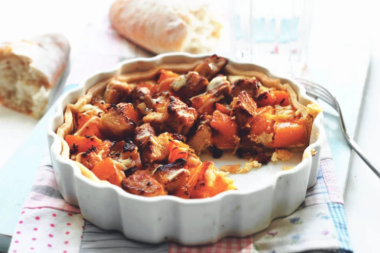 A tart filled with Quorn Pieces, butternut squash, and goat cheese in a white dish with a baguette in the background.