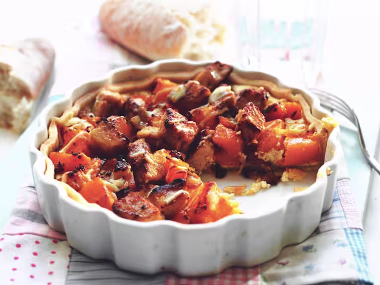 A tart filled with Quorn Pieces, butternut squash, and goat cheese in a white dish with a baguette in the background.
