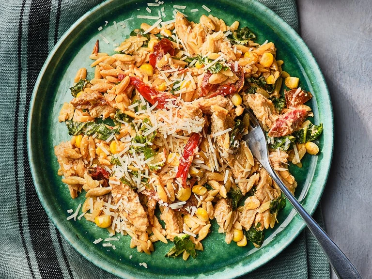 Orzo pasta in a creamy sauce with Quorn Vegetarian Fillets, sundried tomatoes, sweetcorn, kale, and parmesan cheese with a fork on the side. 