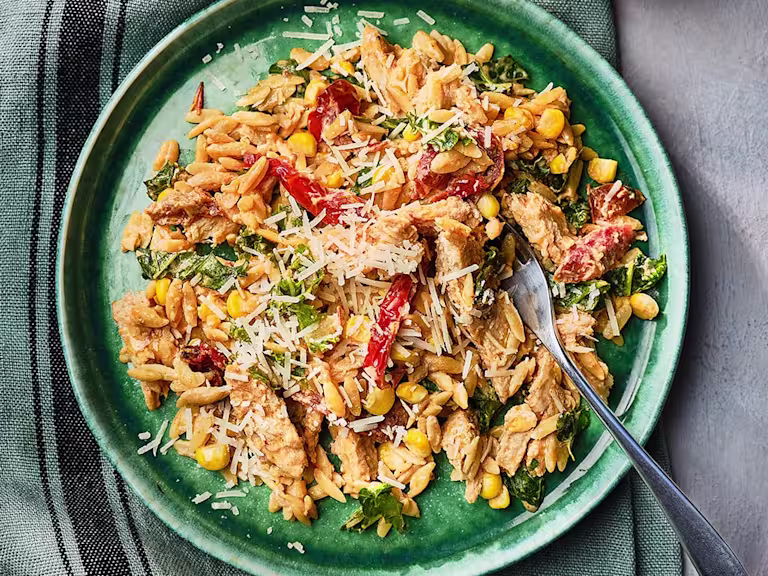 Orzo pasta in a creamy sauce with Quorn Vegetarian Fillets, sundried tomatoes, sweetcorn, kale, and parmesan cheese with a fork on the side.