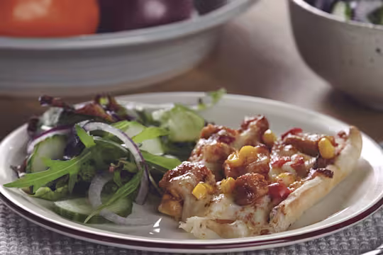 A traybake pizza topped with cheese, sweetcorn, tomatoes, bbq sauce, and Quorn Pieces.