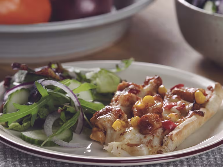A traybake pizza topped with cheese, sweetcorn, tomatoes, bbq sauce, and Quorn Pieces.