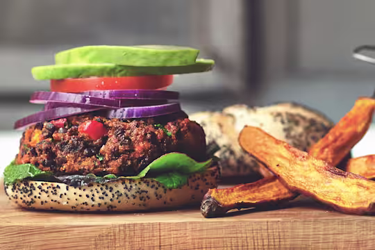 A veggie burger on a poppyseed bun topped with lettuce, tomato, red onions, and avocado with thick-cut fries on the side.