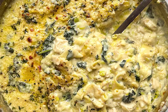 Close up image of a one pot lasagne with a large serving spoon to dish up. The lasagne is topped with melted cheese and herbs.