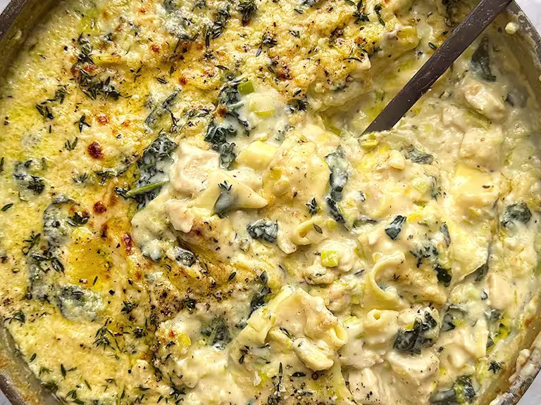 Close up image of a one pot lasagne with a large serving spoon to dish up. The lasagne is topped with melted cheese and herbs.