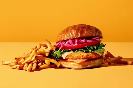 Burgare gjord med Quorn Crispy ChiQin Burger toppad med röd plockad lök serverad med pommes frites.