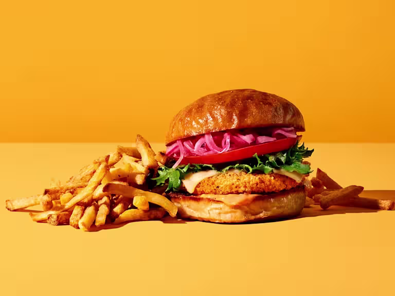 Burgare gjord med Quorn Crispy ChiQin Burger toppad med röd plockad lök serverad med pommes frites.