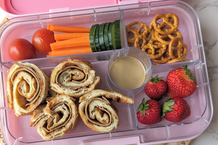 A lunchbox featuring Yorkshire pudding wraps with Quorn Roast Beef Style Slices , pretzels, strawberries, tomatoes, cucumbers and carrots.