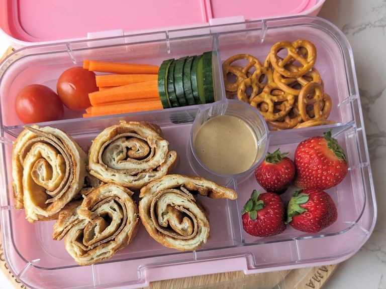 A lunchbox featuring Yorkshire pudding wraps with Quorn Roast Beef Style Slices , pretzels, strawberries, tomatoes, cucumbers and carrots.