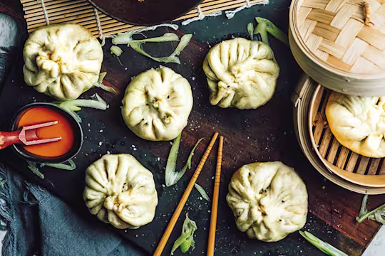 Xiao long bao buns made with Quorn Mince arranged on a board and in a bamboo steamer with a chilli sauce on the side.