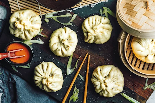 Xiao long bao buns made with Quorn Mince arranged on a board and in a bamboo steamer with a chilli sauce on the side.