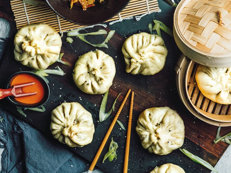 Xiao long bao buns made with Quorn Mince arranged on a board and in a bamboo steamer with a chilli sauce on the side.