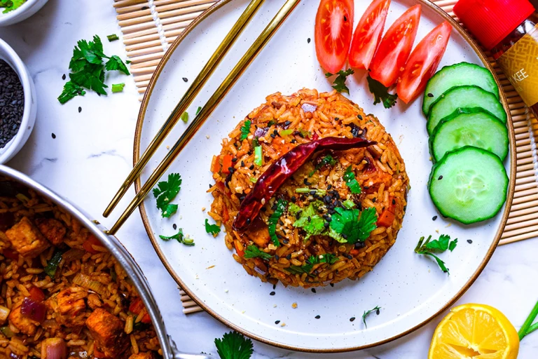 Plate of vegan nasi goreng with wedges of tomato and slices of cucumber and cutlery