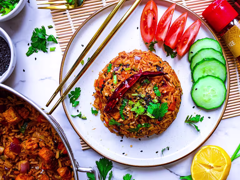 Plate of vegan nasi goreng with wedges of tomato and slices of cucumber and cutlery