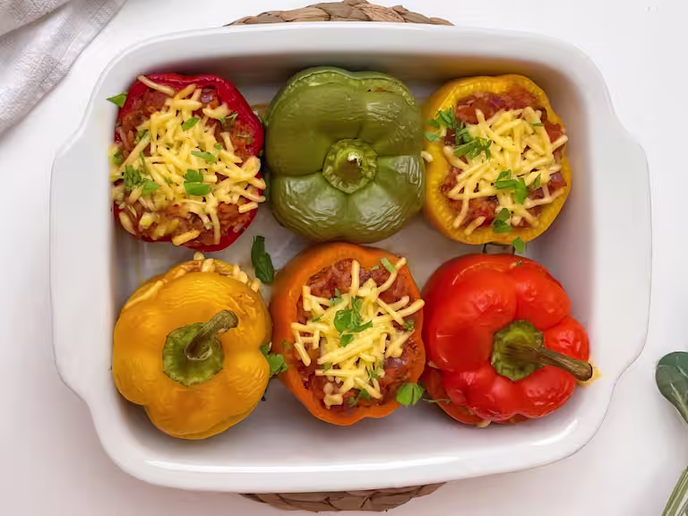 Six stuffed peppers served in a white dish.