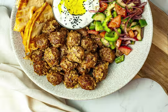 Vegetarian keftedes served on a spotted dish with a side salad of cucumber and tomato, pitta bread and tzatziki.