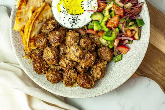 Vegetarian keftedes served on a spotted dish with a side salad of cucumber and tomato, pitta bread and tzatziki.