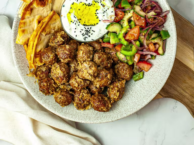 Vegetarian keftedes served on a spotted dish with a side salad of cucumber and tomato, pitta bread and tzatziki.